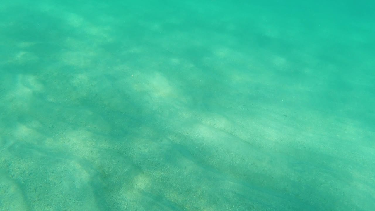 Shallow turquoise sea with faint darker sand shapes.