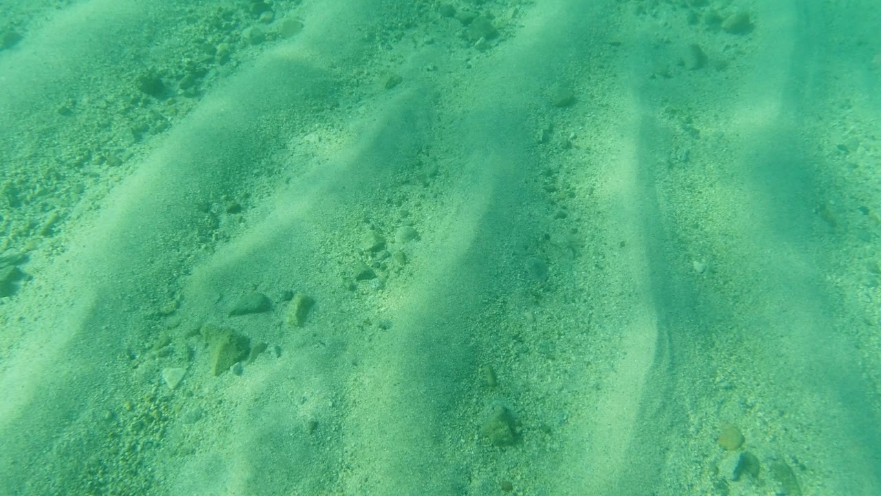 Clear turquoise water in Los Cabos, Mexico covers pale rippled sand and small stones, with no visible people at the opening moment.
