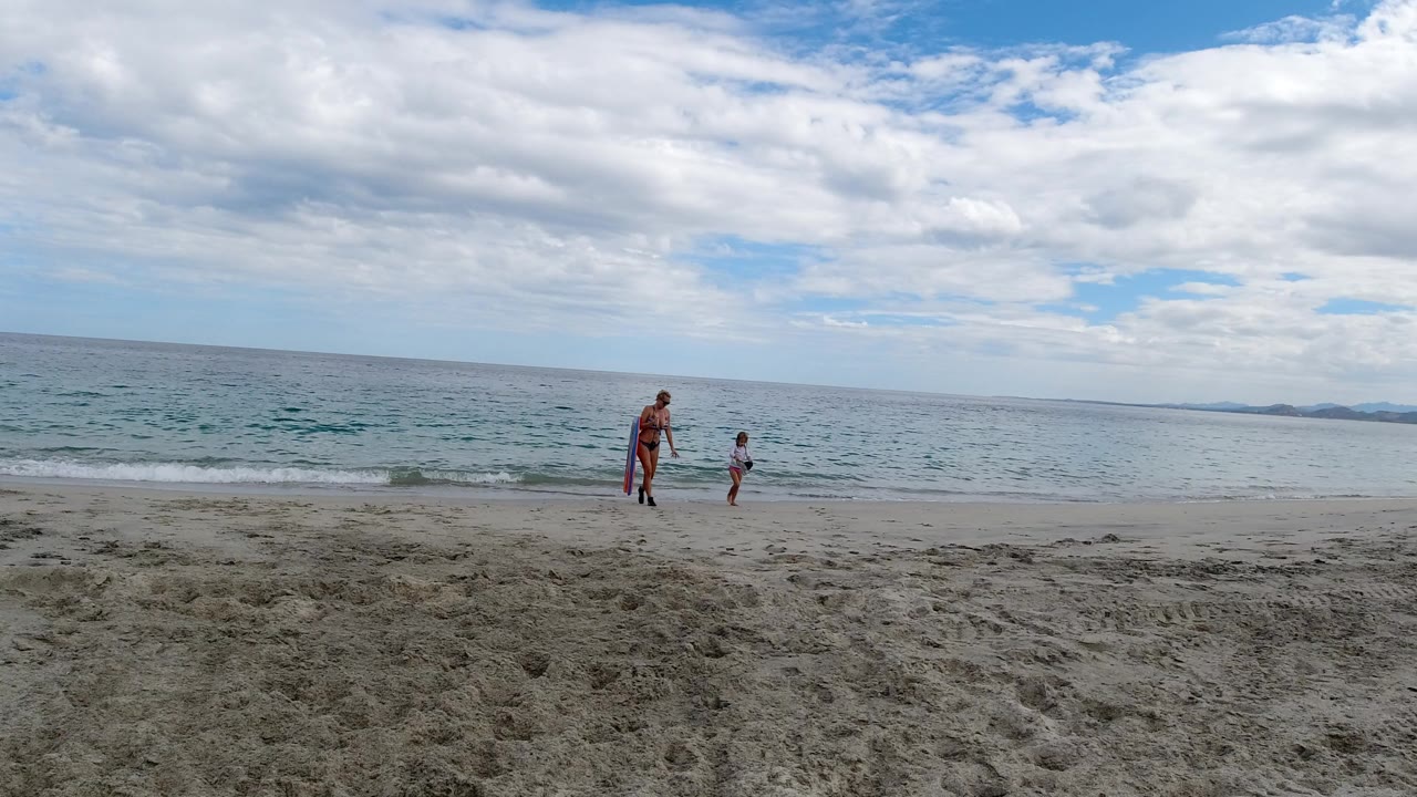 Woman with red towel and child near the surf on a beach.
