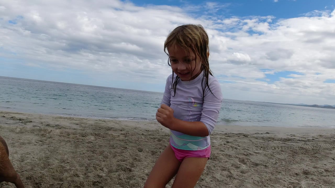 Young girl on sandy beach with ocean behind her.