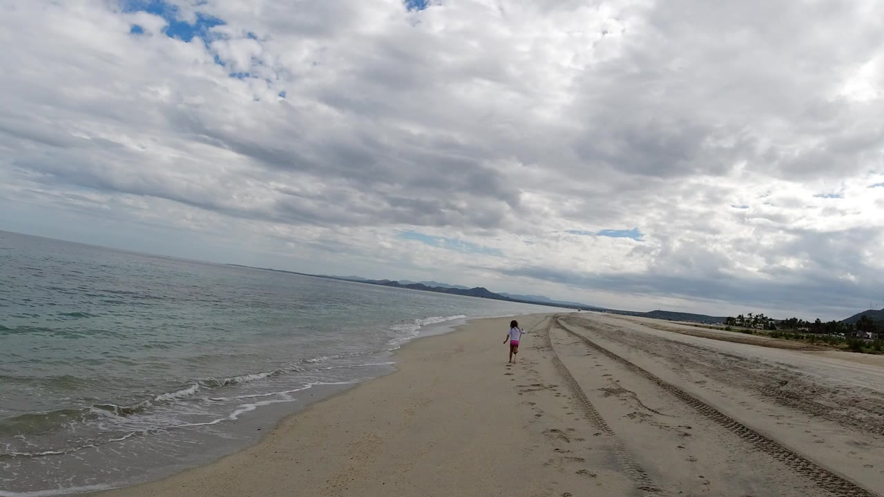 Child walking on a wide beach beside small ocean waves