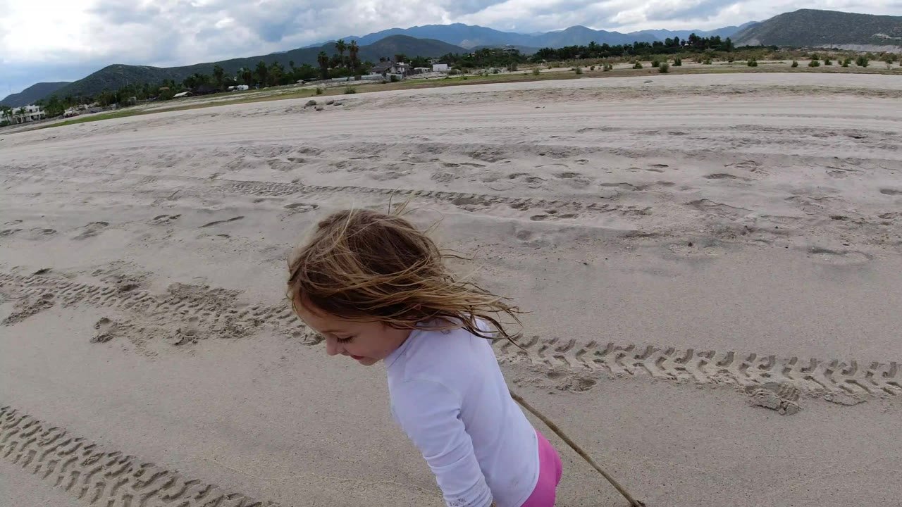 Young girl close to camera on sandy beach with hills behind her.