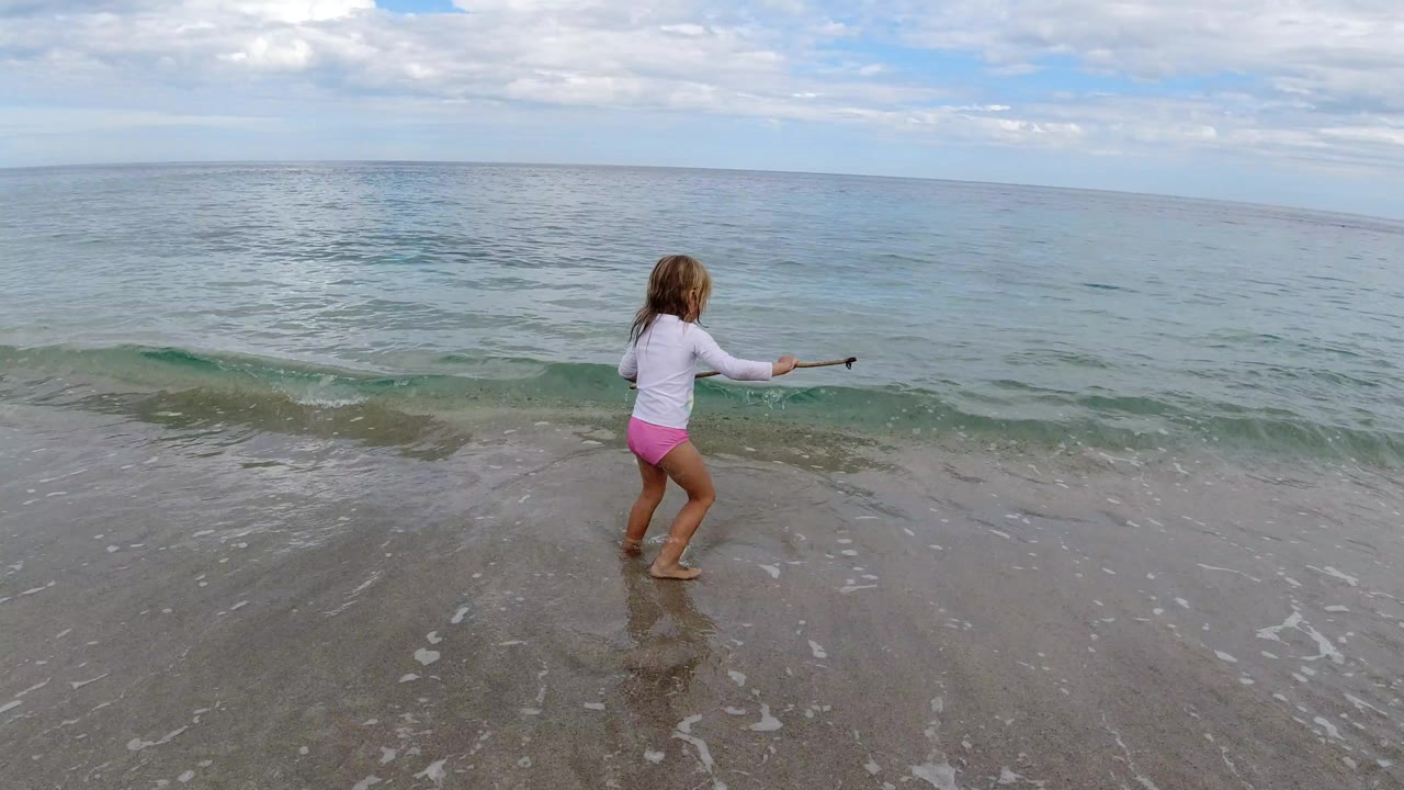 The girl remains near the shoreline in Los Cabos, Mexico, with her arm extended and a low green wave forming behind her.