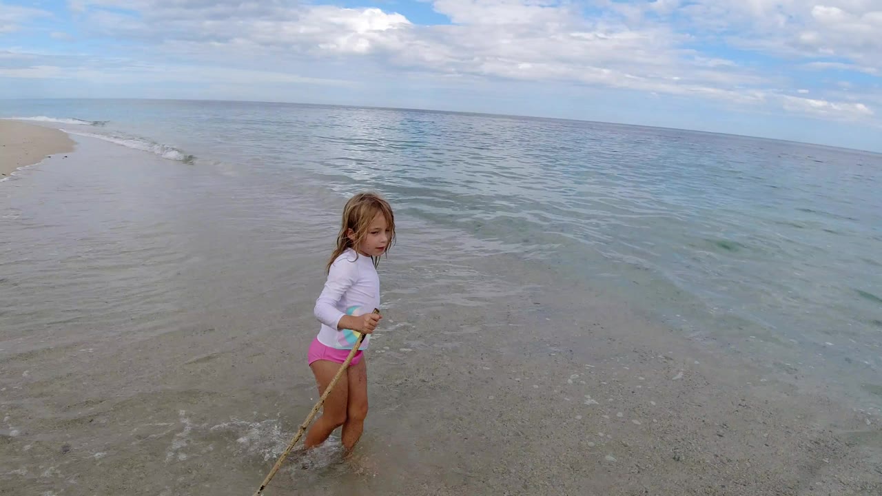Young girl holding a stick at the edge of the surf.