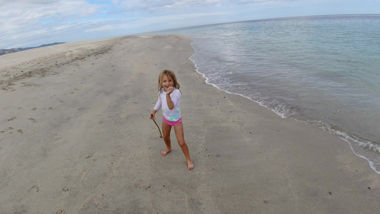 Child standing barefoot on a sandy beach beside shallow surf.