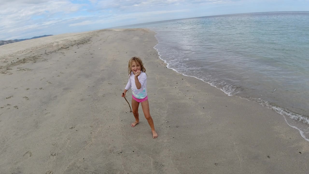 The child remains near center frame in Los Cabos, Mexico, as the waterline curves diagonally past the sandbar on the right.