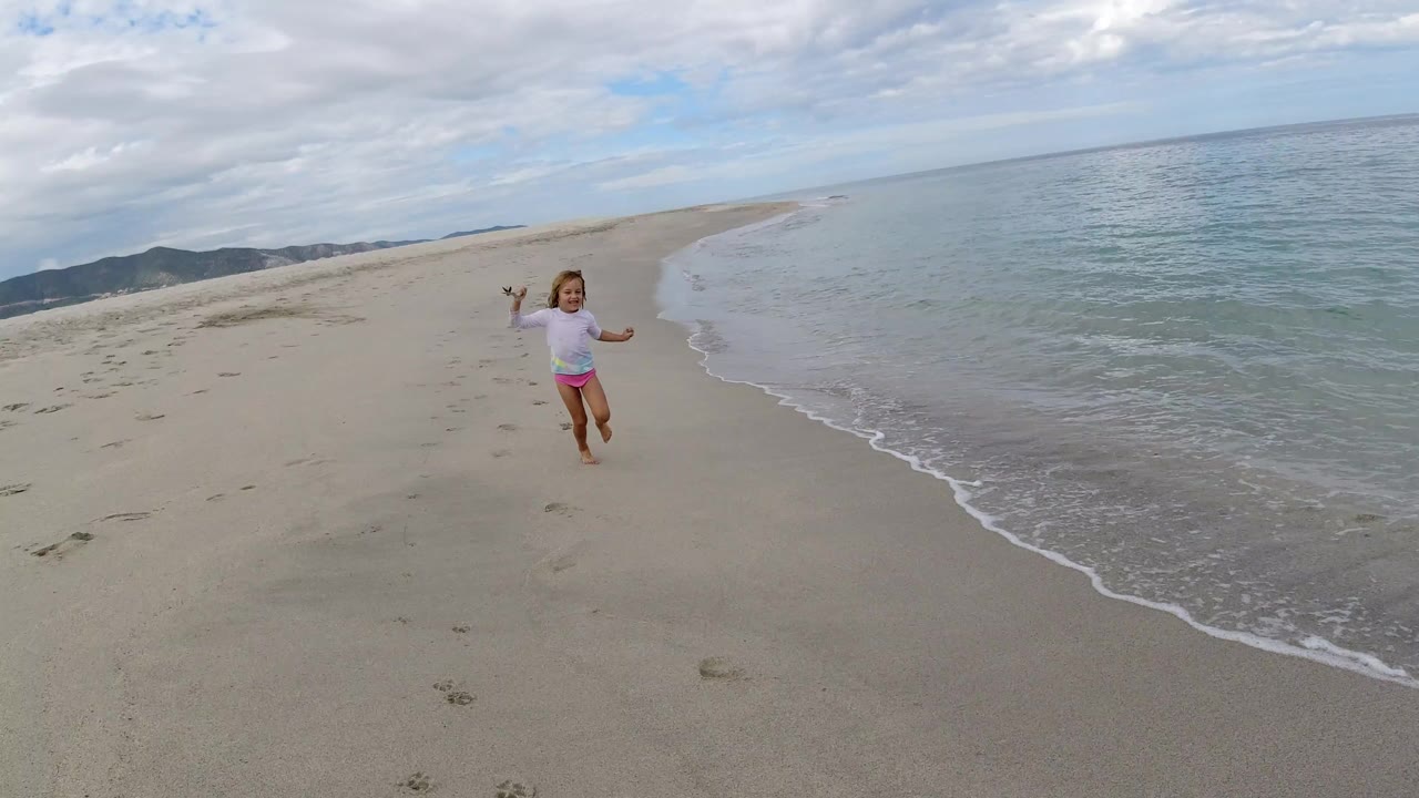 Young girl running on sandy beach near the waterline.