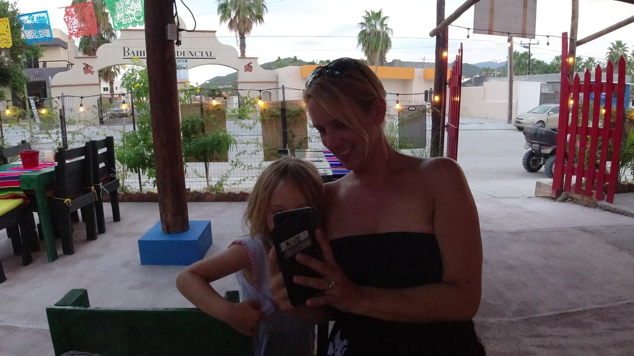 Adult woman and child look at a phone on an outdoor patio.