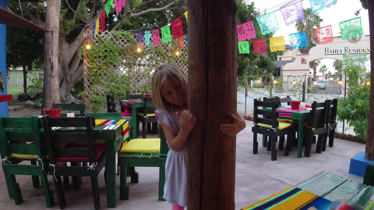 Young girl peeking from behind a wooden post on a colorful patio.