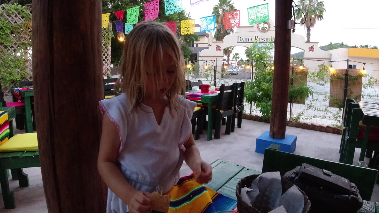 Child seated at a patio table under colorful paper banners.