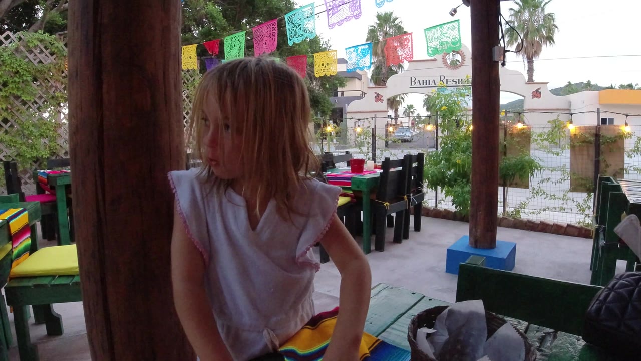 Blond child standing on a covered deck with colorful party banners overhead.