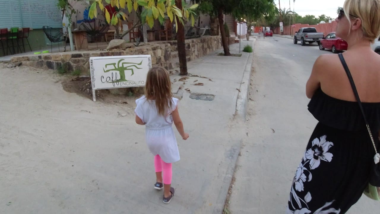 Little girl and adult woman walking along a sidewalk near a roadside sign.