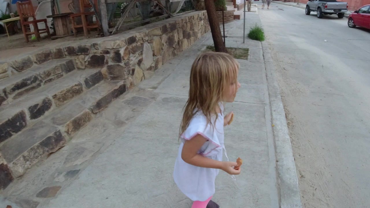 Young girl walking beside a stone wall on a sidewalk near a road.