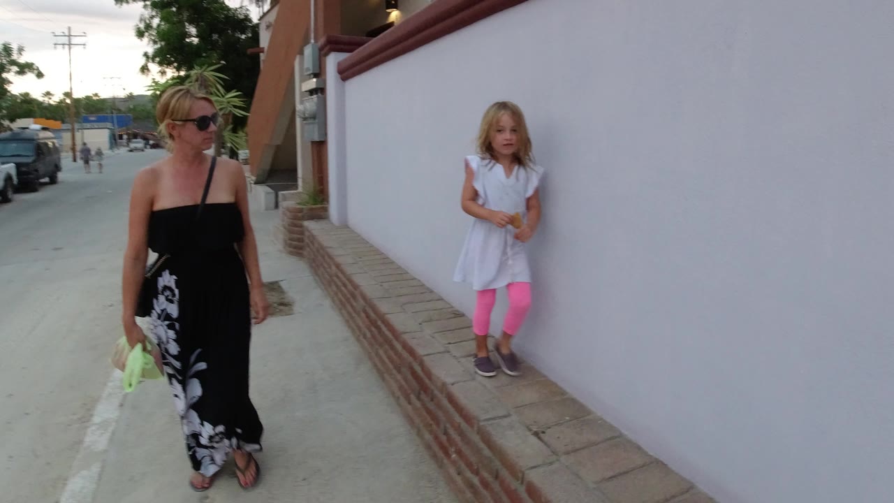 Woman and young girl beside a white wall on a sidewalk.