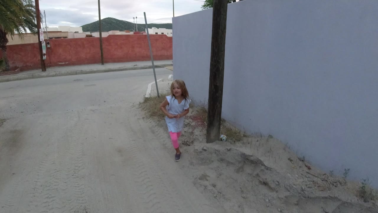 Young girl running on a sandy alley near a pale wall.
