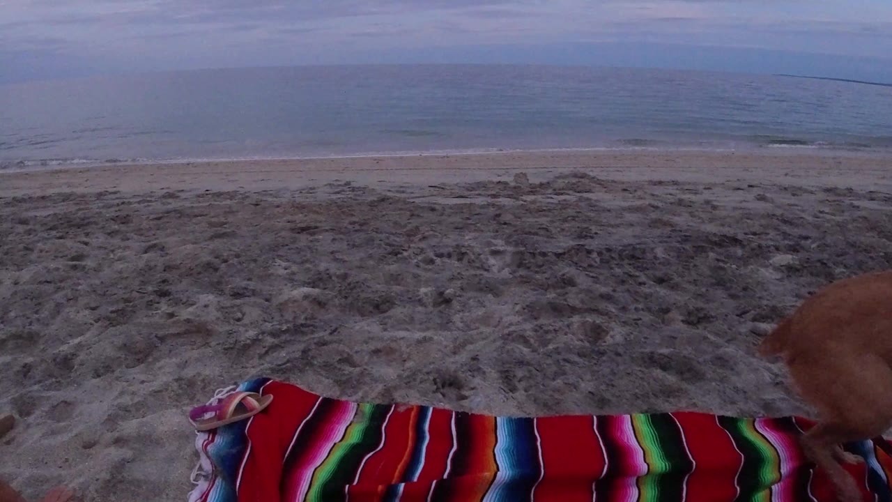 Striped beach blanket on sand with ocean beyond.