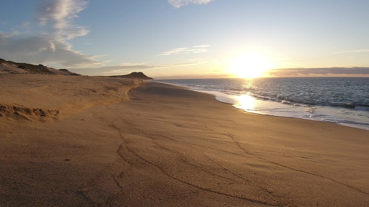 Empty beach with ocean waves and bright sun near the horizon
