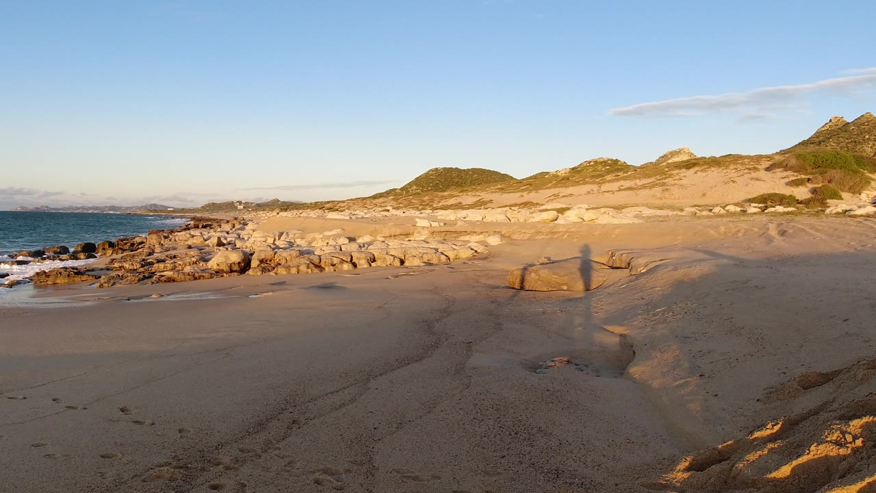 Rocky coast, sand, ocean, and sunlit hills.