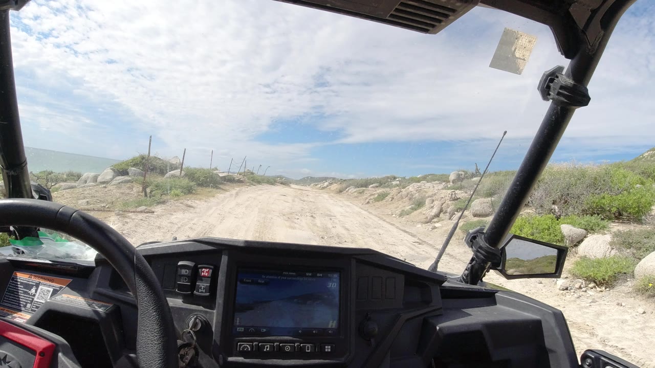Off-road vehicle cockpit facing a dusty coastal dirt road.