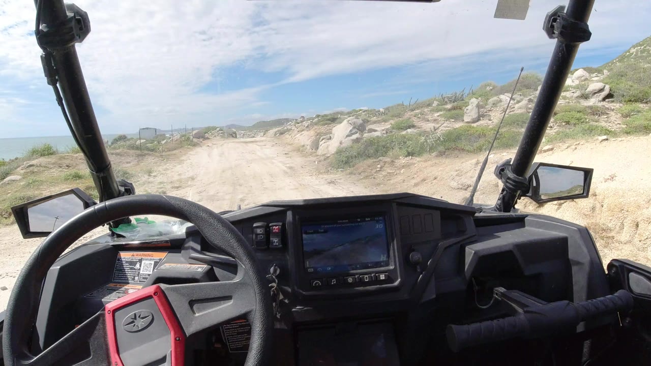 Vehicle interior looking down a sandy rocky track under a bright sky.