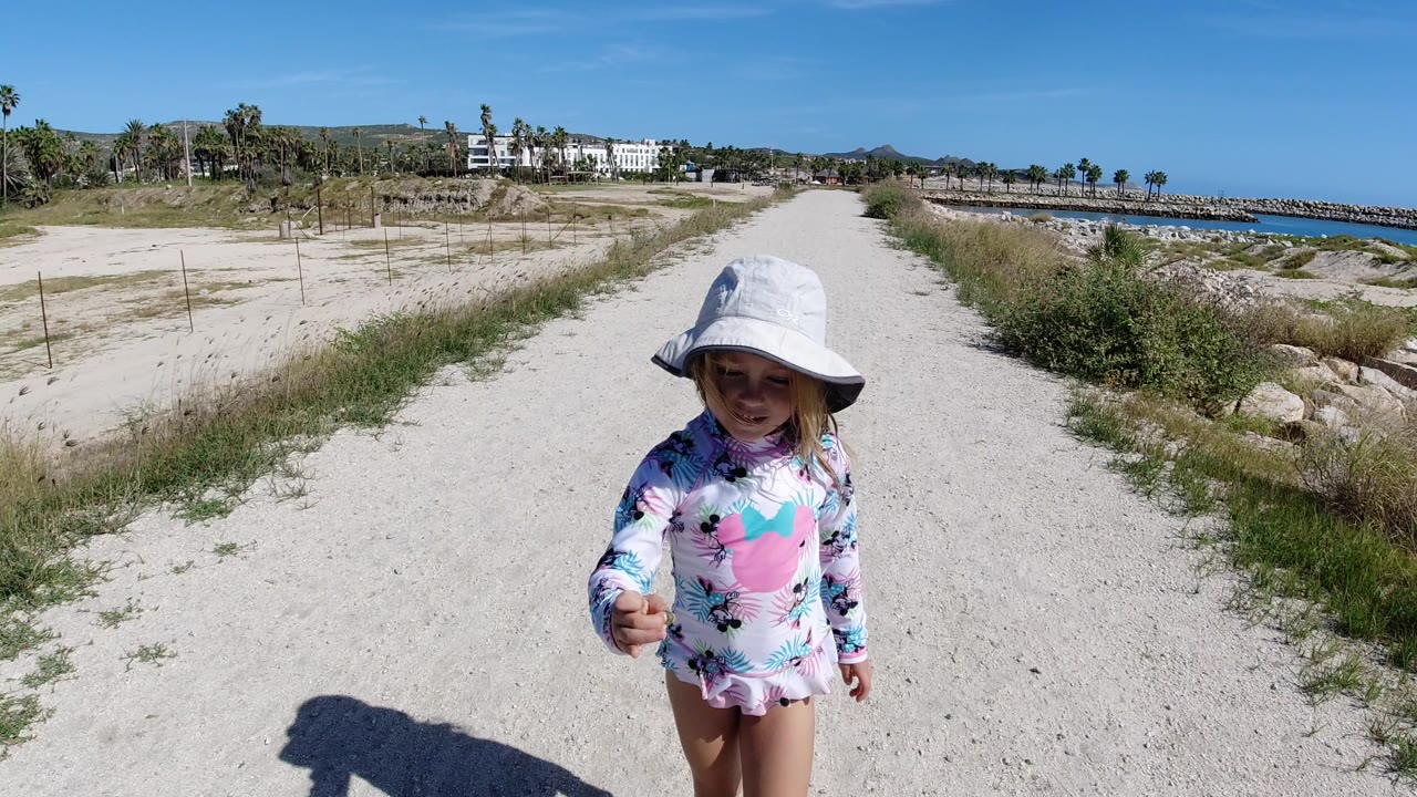 Young girl in a white sun hat on a rough coastal road.