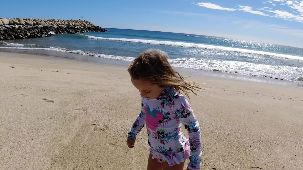 Young girl walking on sand near ocean waves