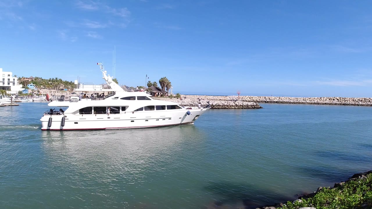 White yacht on calm harbor water near a rock breakwater.