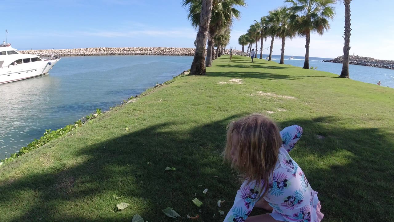 Child near grassy waterfront with palms and yacht