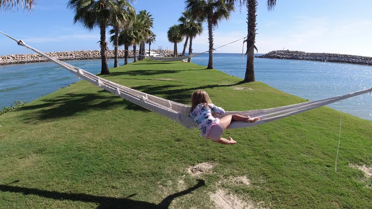 One second in, the child remains reclined in the hammock on the Los Cabos waterfront lawn while sun sparkles on the blue water behind the palms.