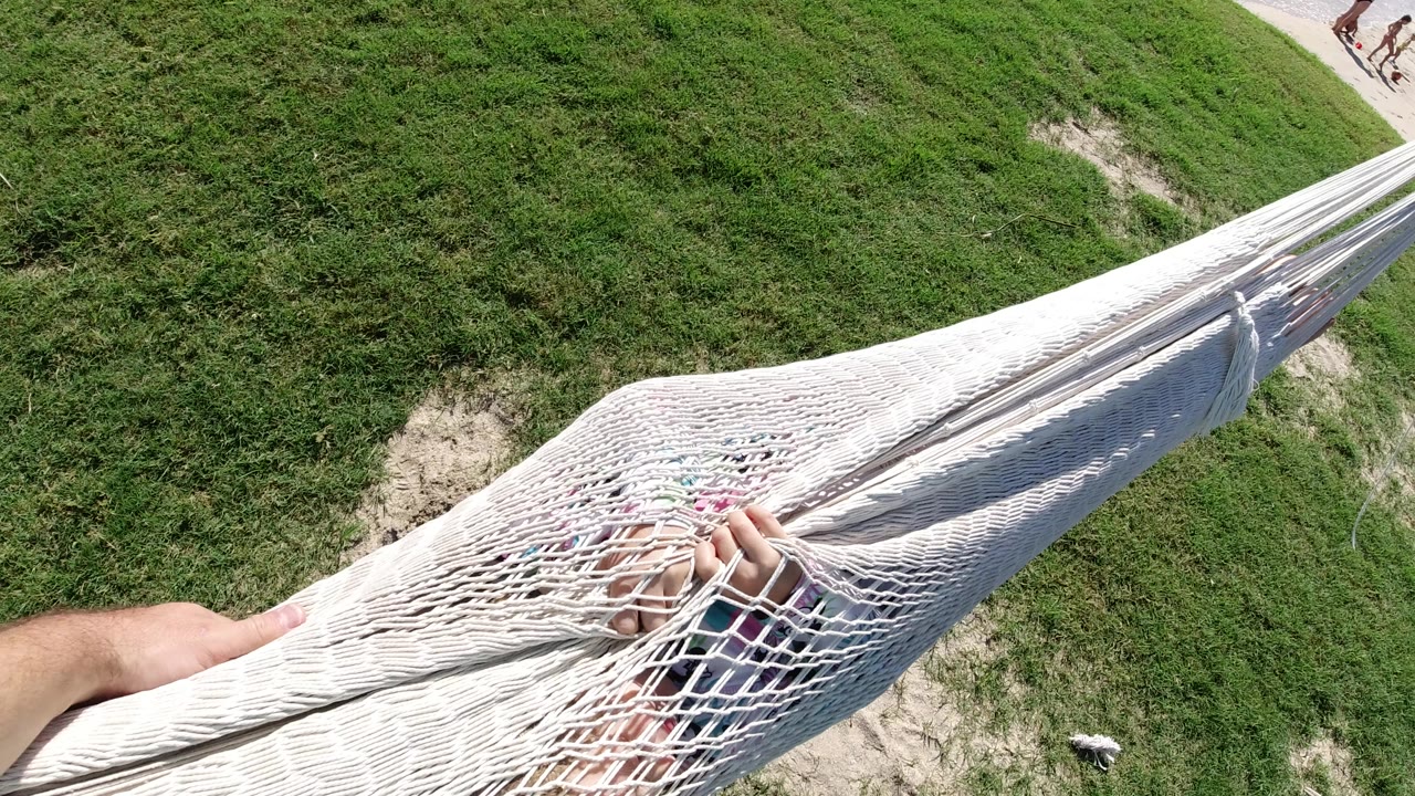 White rope hammock over grass with hands and feet visible through the net.