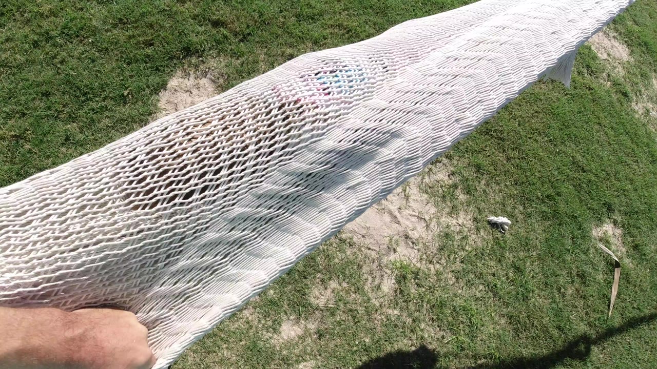 Overhead view in Los Cabos, Mexico of a white rope swing stretched over grass and sand, with an adult hand partly visible at the lower left.