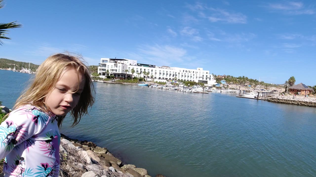 Young girl beside blue water with white waterfront buildings behind her.