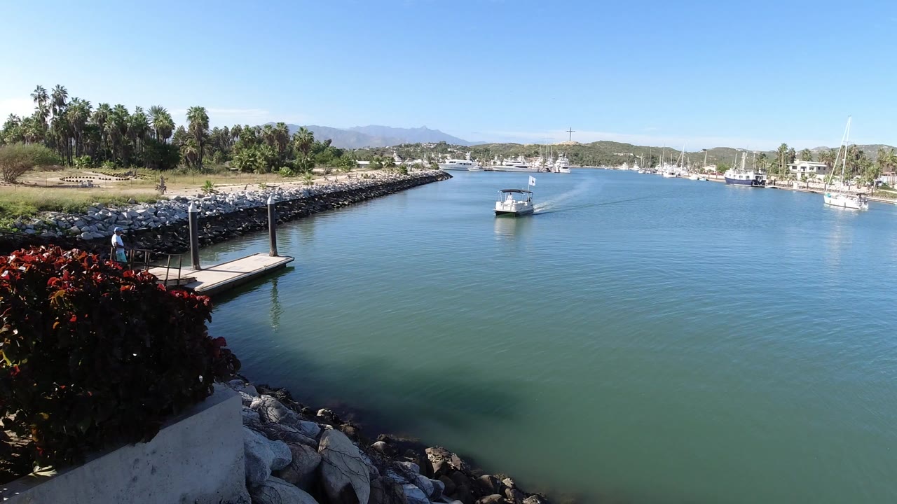 Small boat in a calm water channel beside a rock breakwater and dock.