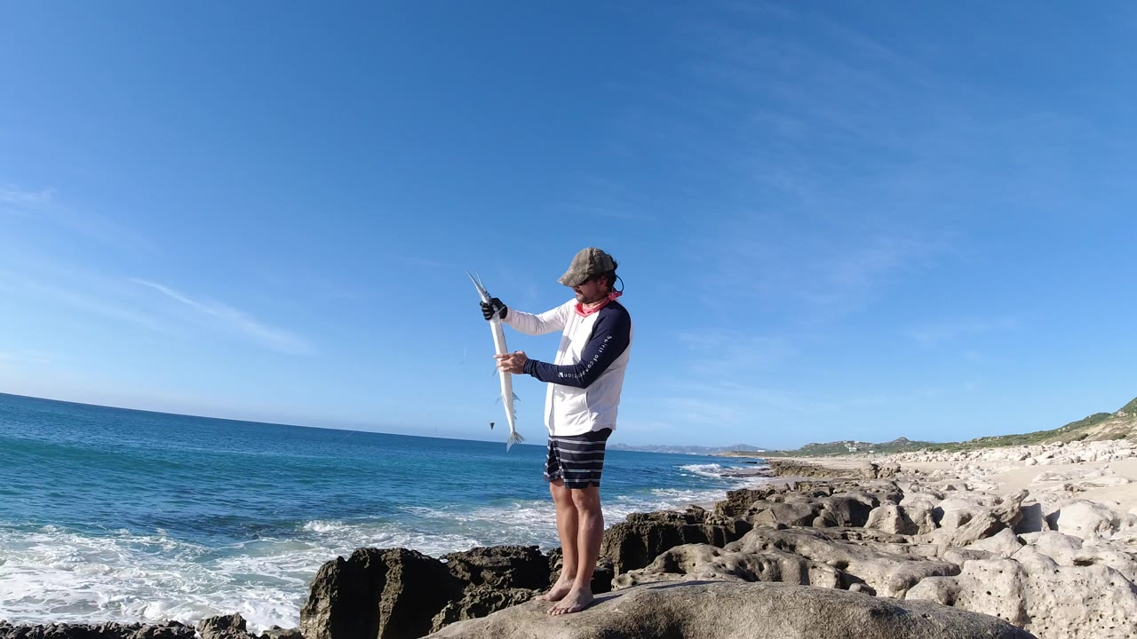 Man standing on coastal rocks holding a fishing rod beside the ocean.