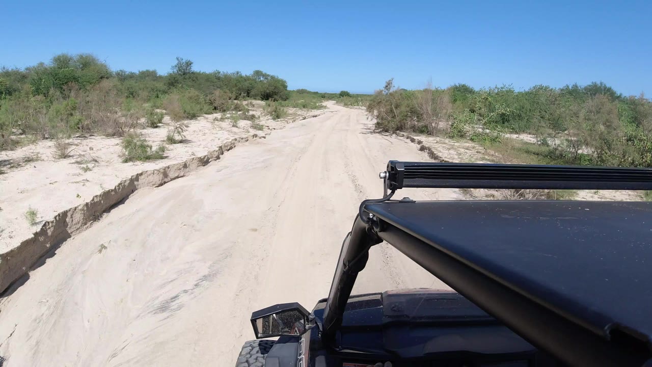Sandy dirt road ahead of a Jeep roof under a clear blue sky.
