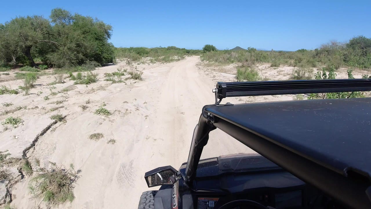 Sandy desert road seen over the front of a black vehicle.