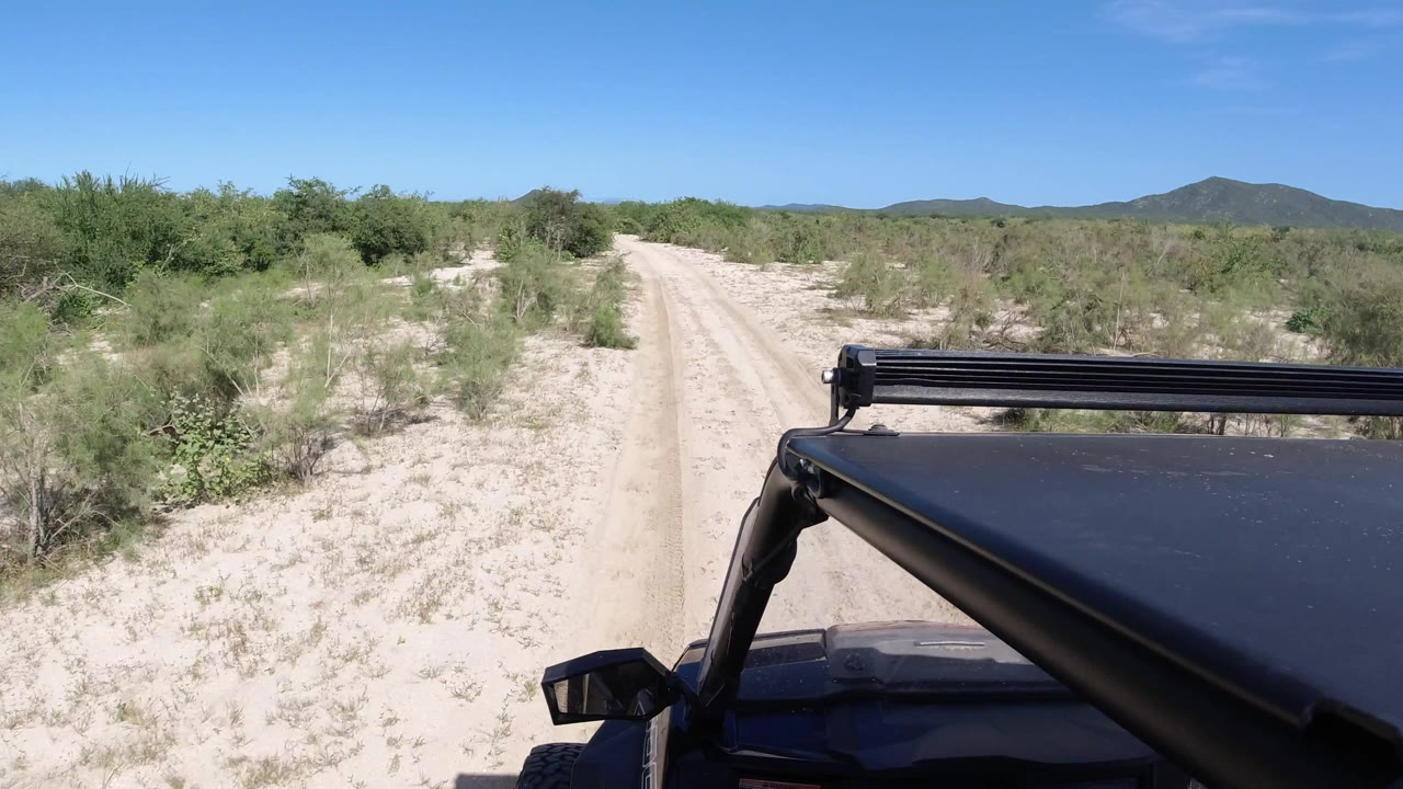 Unpaved desert road with vehicle roof entering from the right.