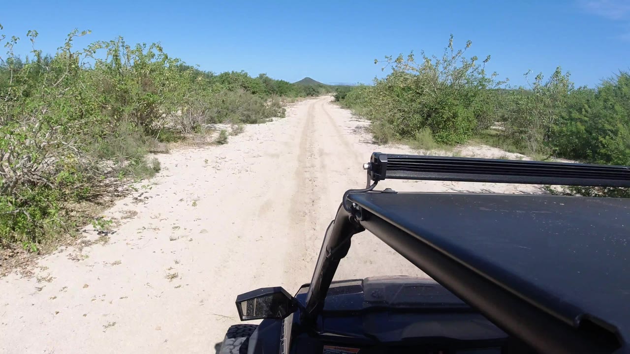 Sandy road curves through scrub with Jeep hood and light bar at right.