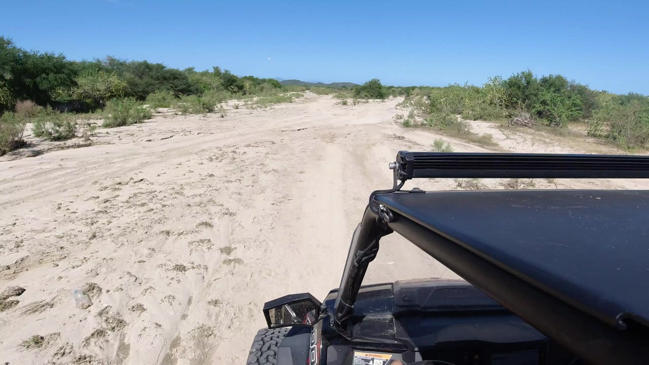 Sandy trail with green brush and off-road vehicle foreground