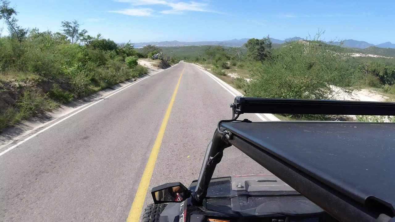 Forward view down a paved road with vehicle roof bar in foreground