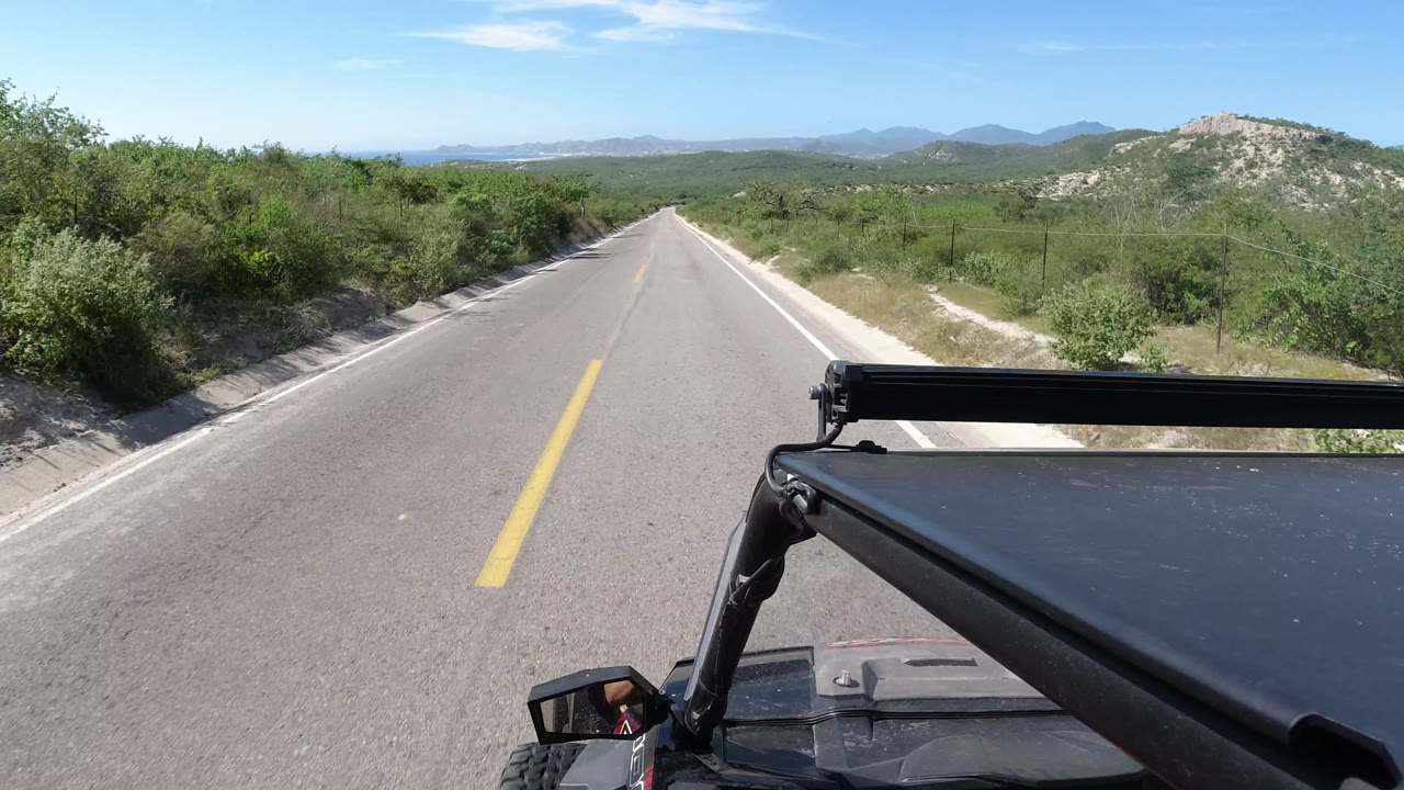 Vehicle-mounted road view with brush and rocky hill to the right.