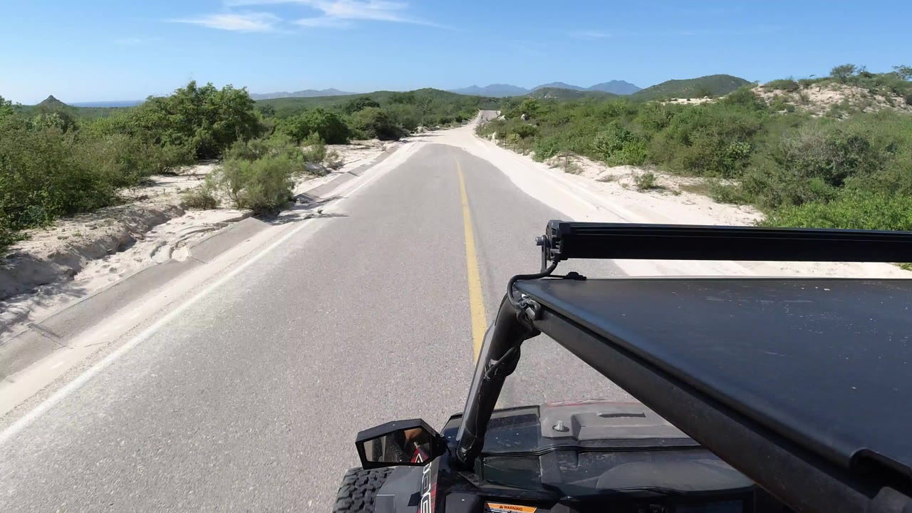 Vehicle POV on a paved road bordered by sand and shrubs