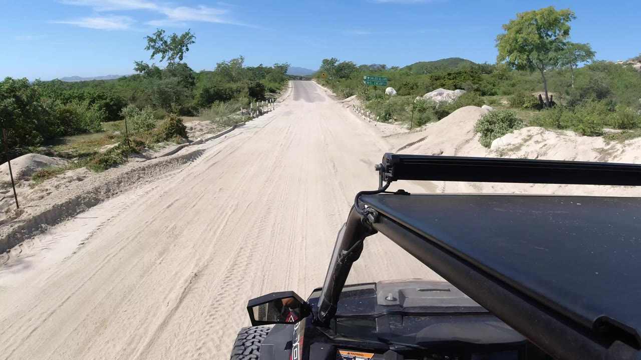 Jeep hood on a pale dirt road with green brush and blue sky.