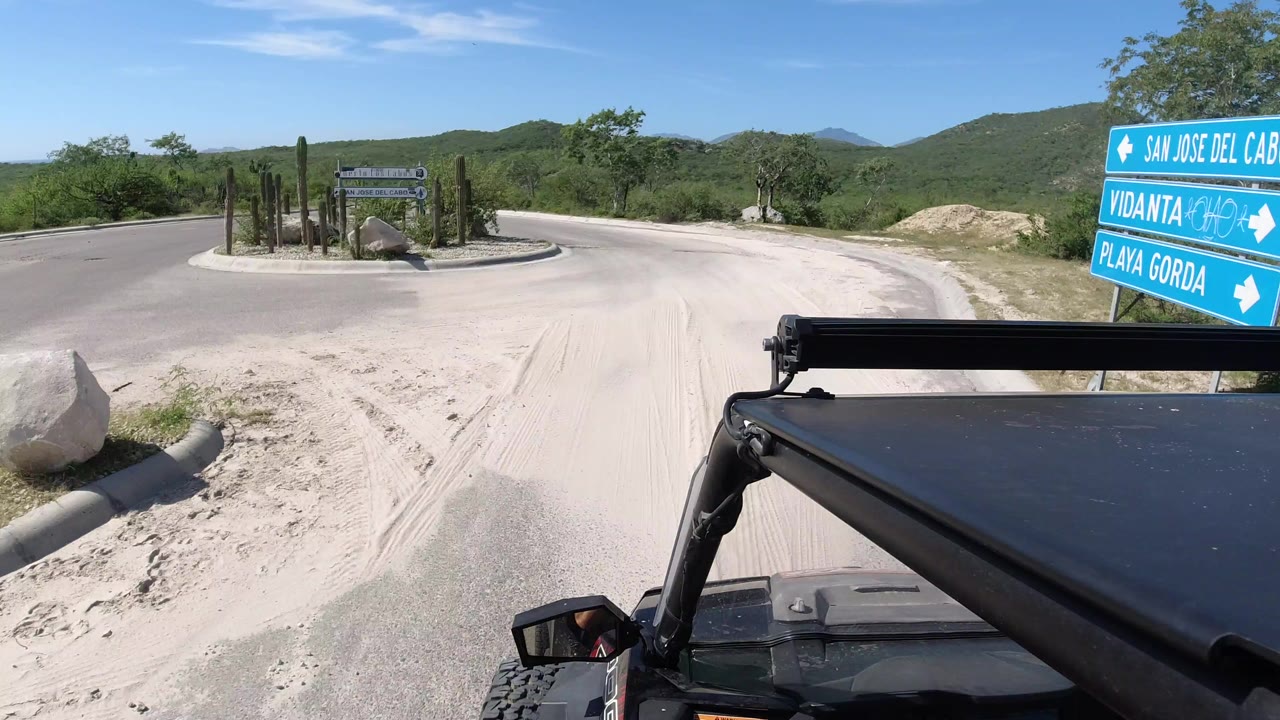 Jeep-mounted view of a road junction with blue directional signs and green hills.