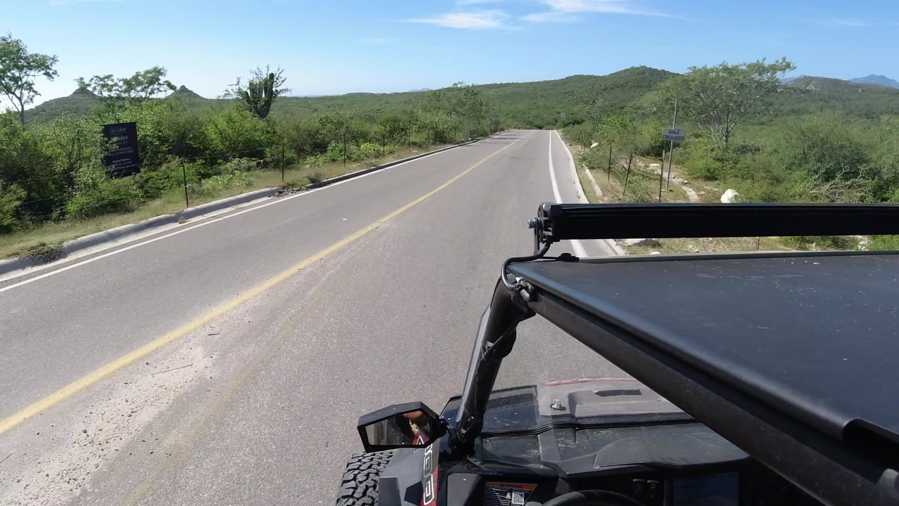 Rural highway passing green brush with the Jeep roof filling the lower right.