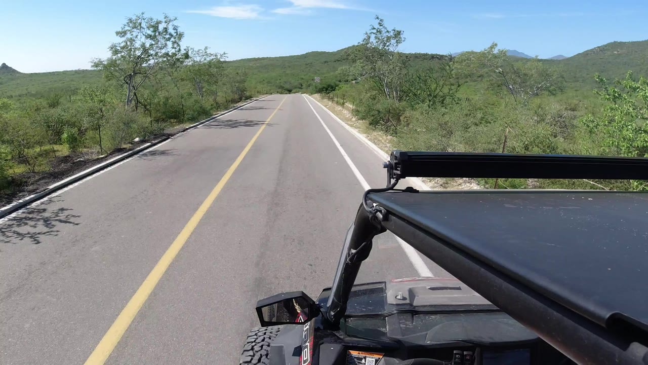 Paved road ahead from a Wrangler with scrub trees and low hills.