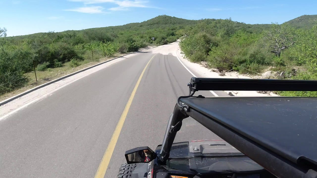 Paved road leading toward green hills with vehicle frame in foreground