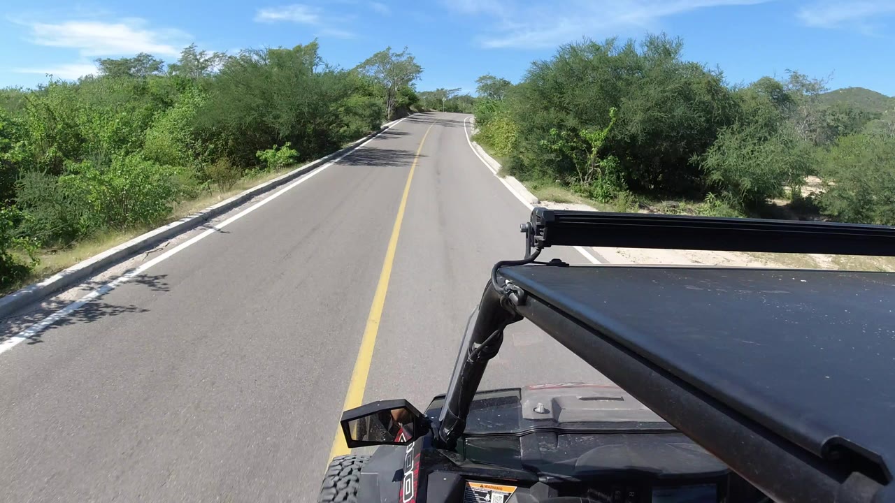 Paved road ahead with yellow centerline and open vehicle roof in foreground.