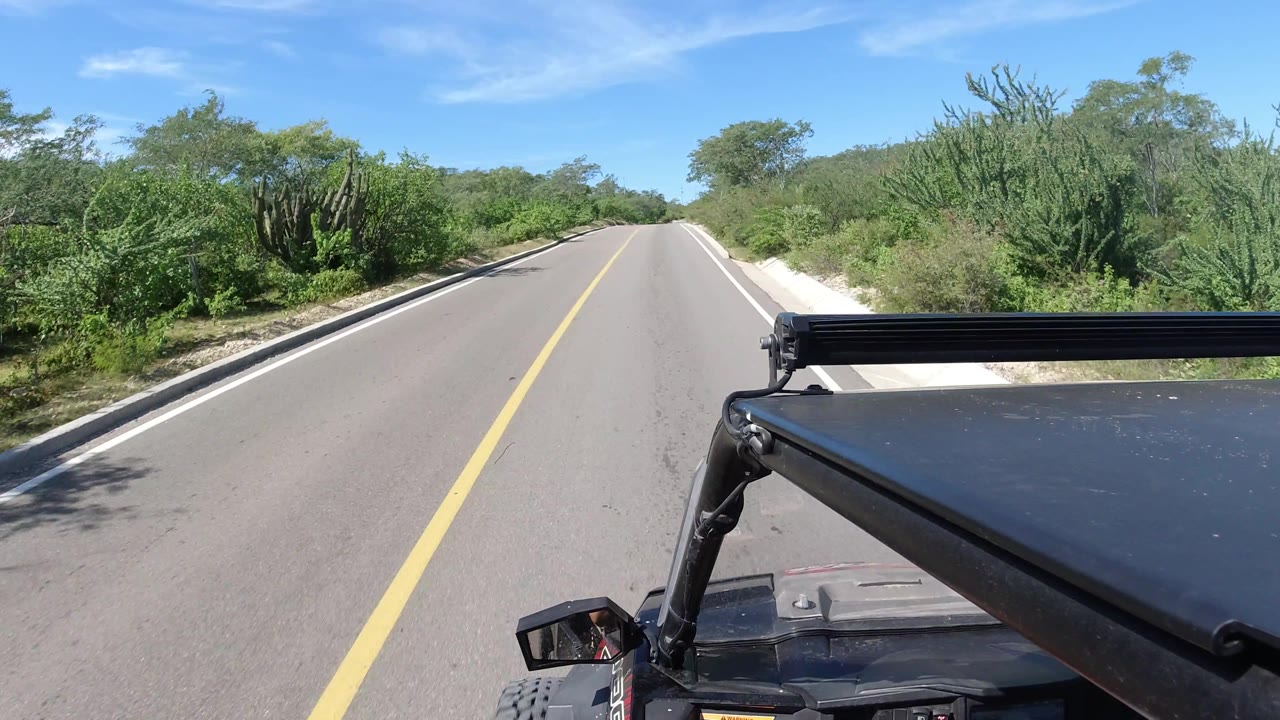 Empty paved road with desert-green vegetation and vehicle hardware in the foreground.