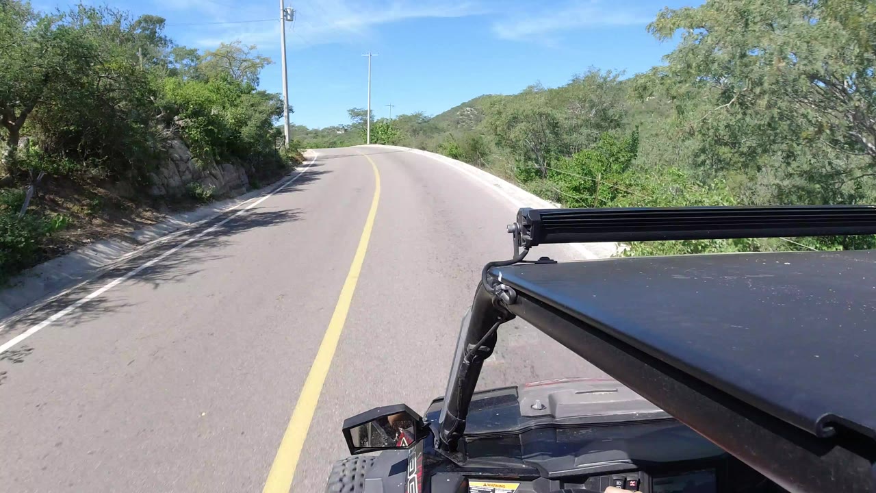 Roof-mounted Jeep view on a curved paved road with green hills.
